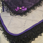 Quilted purple snuggle blanket with black lace trim on a beige background