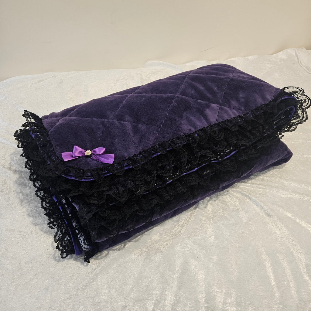 Purple snuggle blanket with black lace and a purple bow on a textured white surface