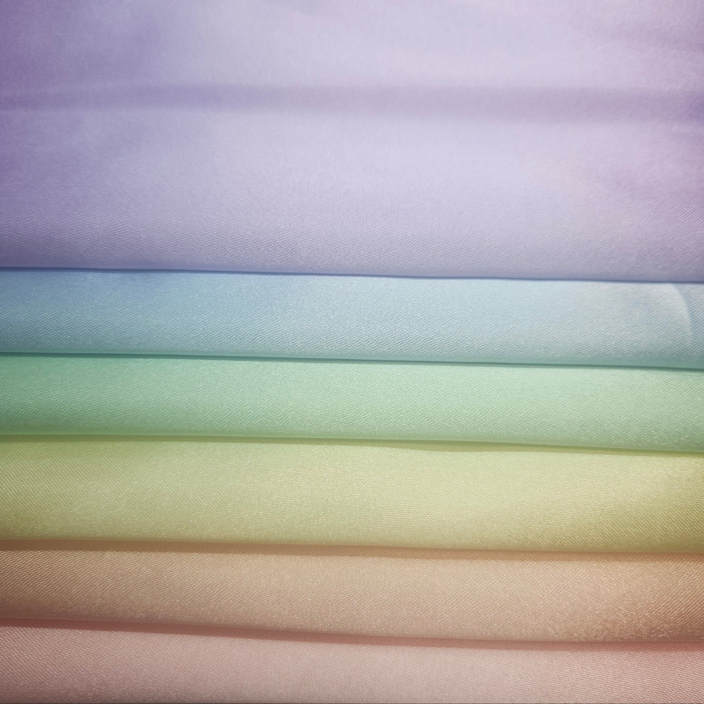 Stack of folded satin fabric swatches in pastel colors.