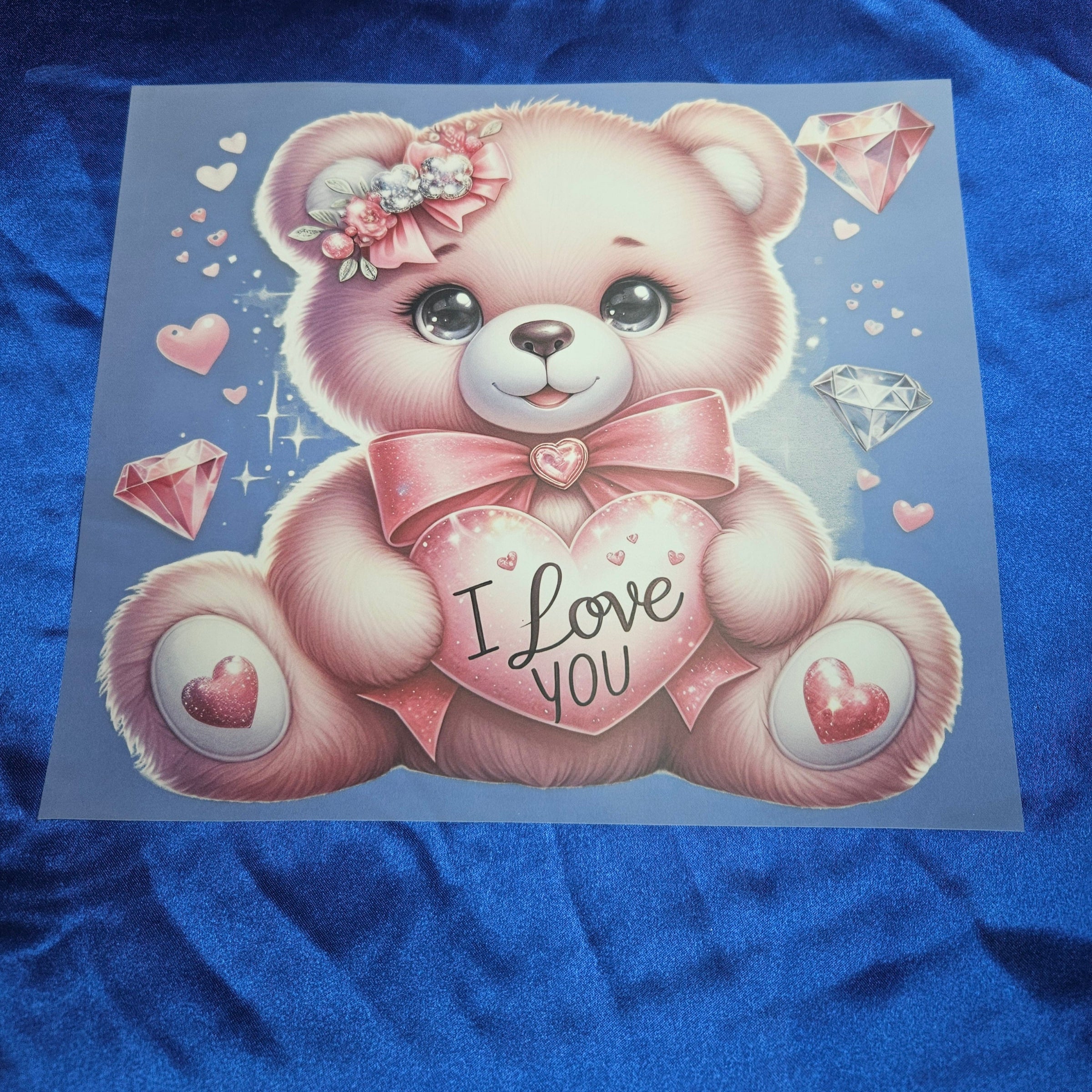 Cartoon teddy bear with 'I Love You' heart applique on a blue satin background