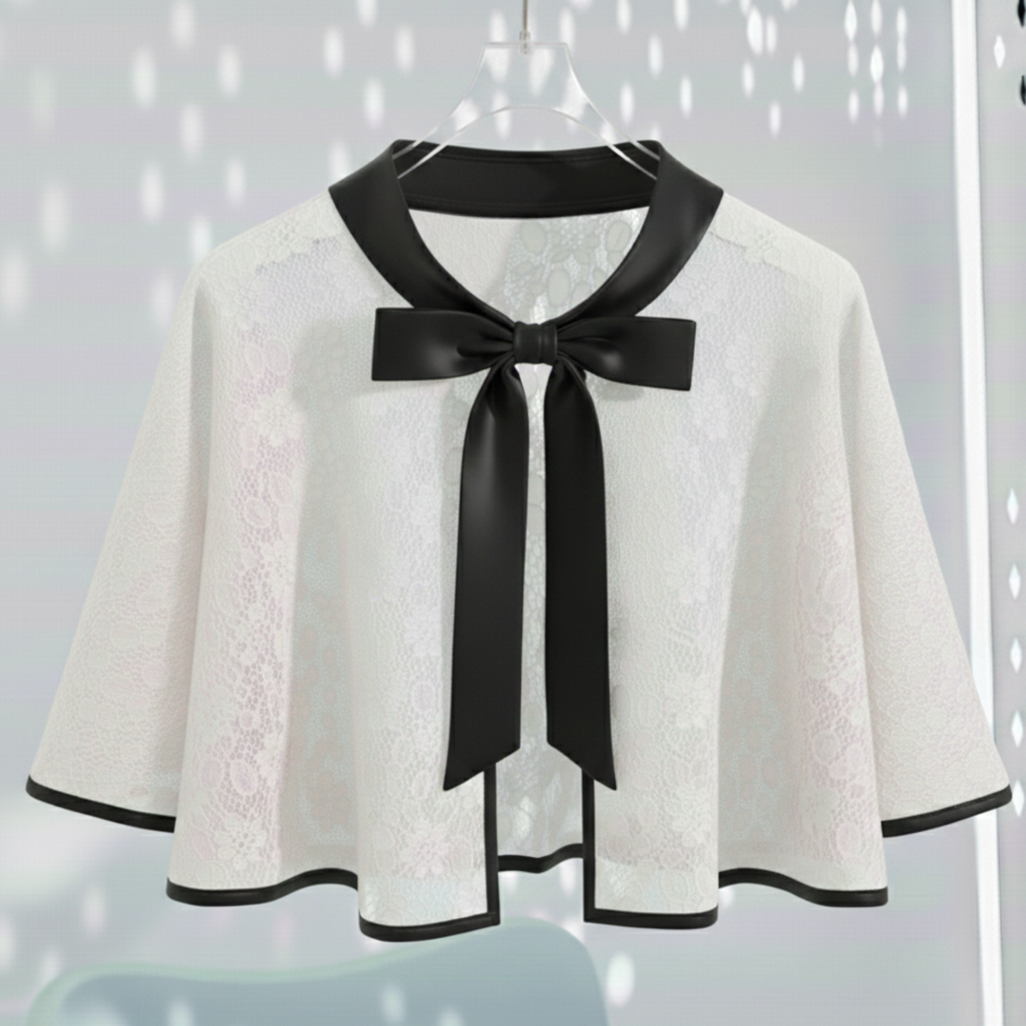 White lace Cape with black Satin Bow Tie on a hanger against a light gray background