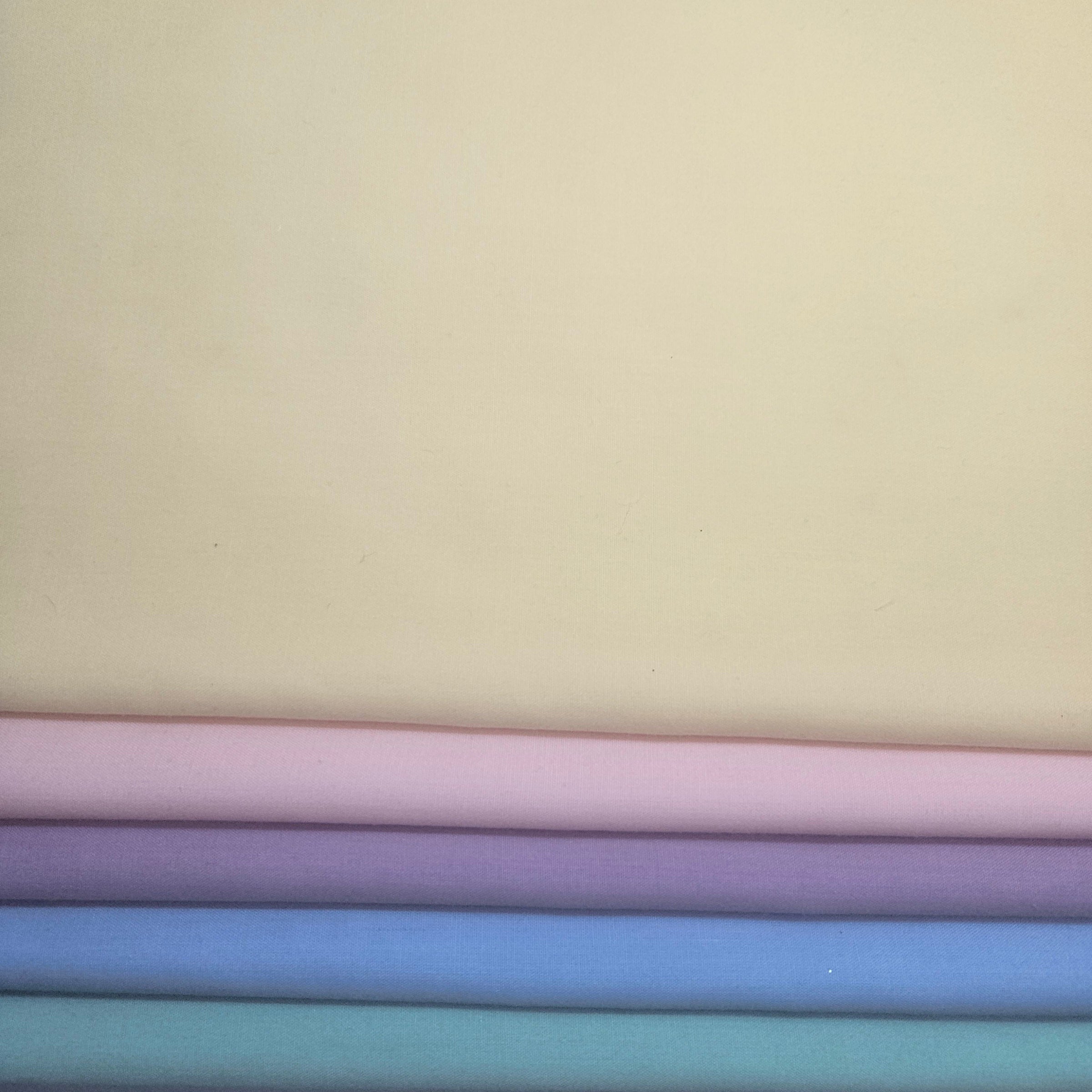Stack of pastel-colored fabrics including pink, yellow, purple, blue, and green broadcloth.