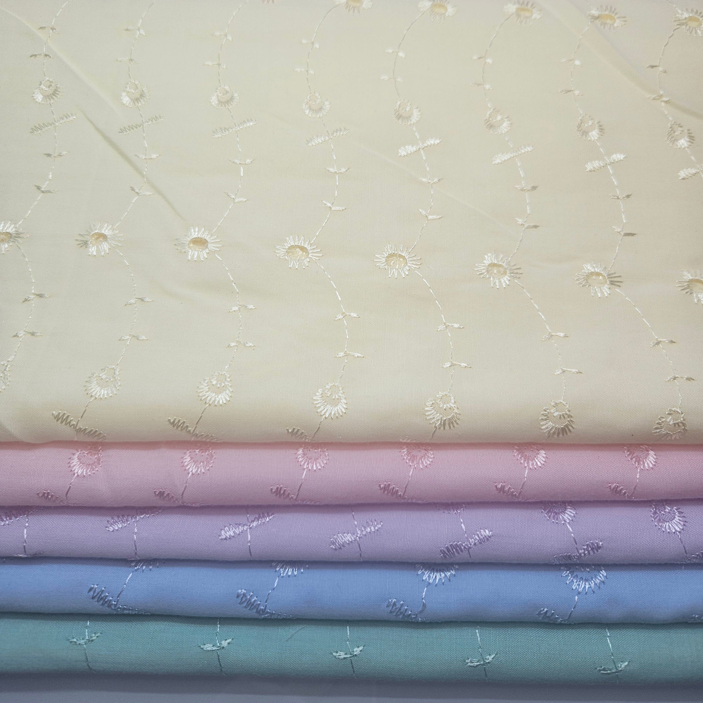 Stack of fabric swatches with floral patterns on yellow eyelet background