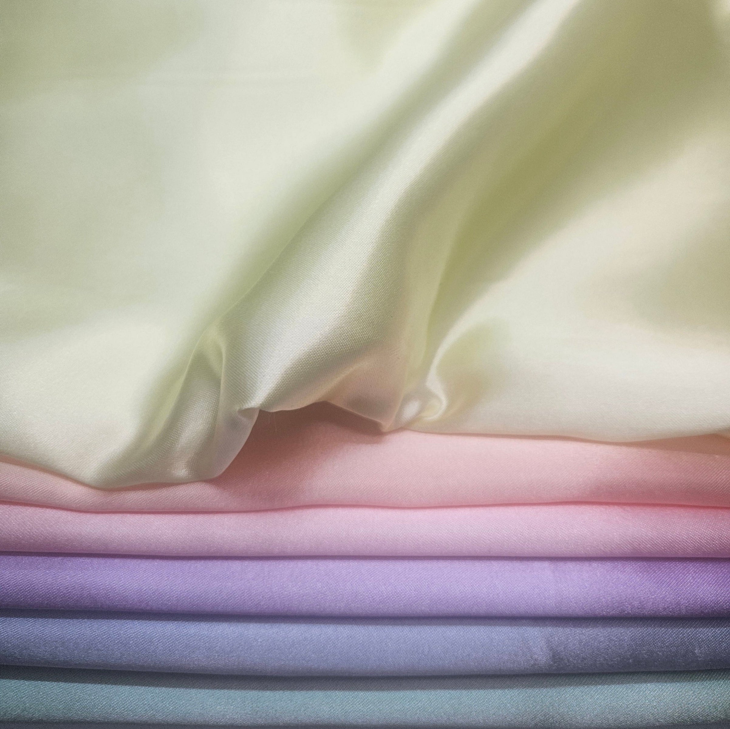 Stack of pastel-colored fabrics including yellow, peach, pink, purple, blue, & mint green
