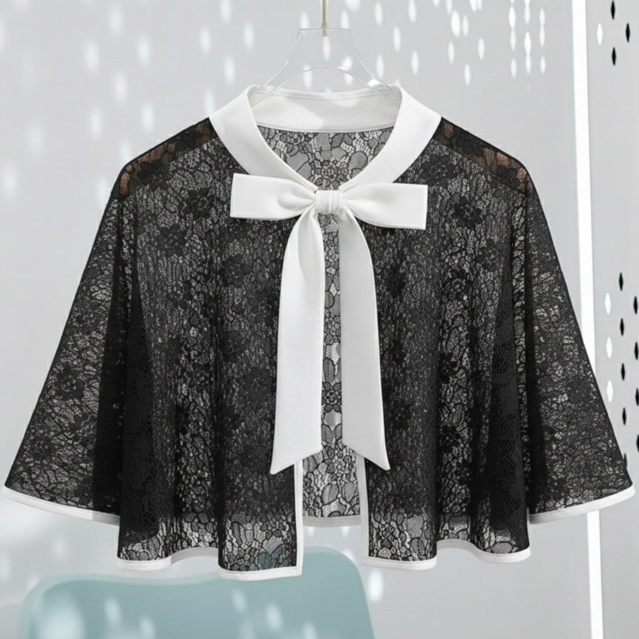 Black lace cape with a white bow on a light gray background