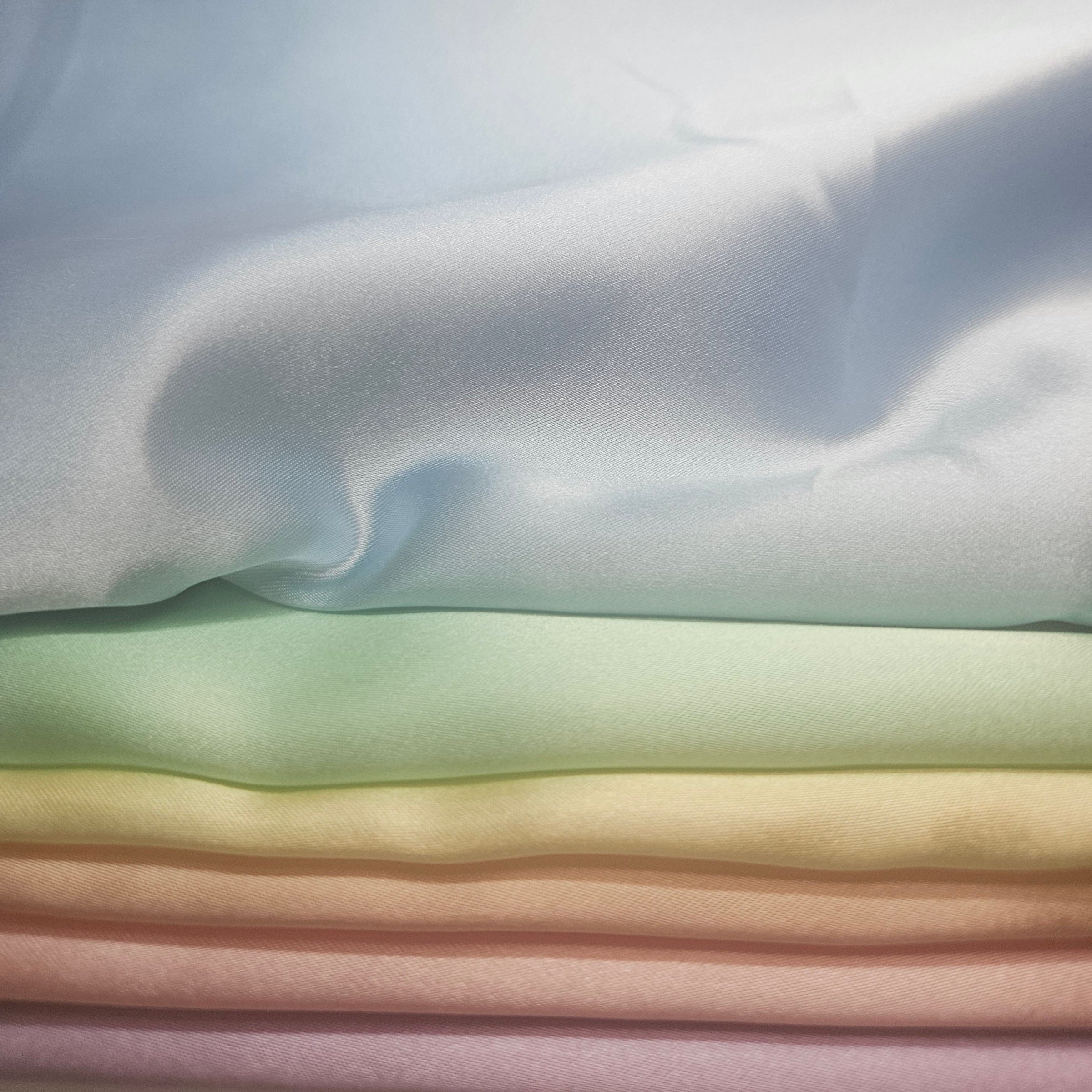Stack of pastel-colored fabrics including yellow, peach, pink, purple, blue, & mint green