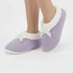 Lavender fleece slippers with white bows worn by a person on a light gray background