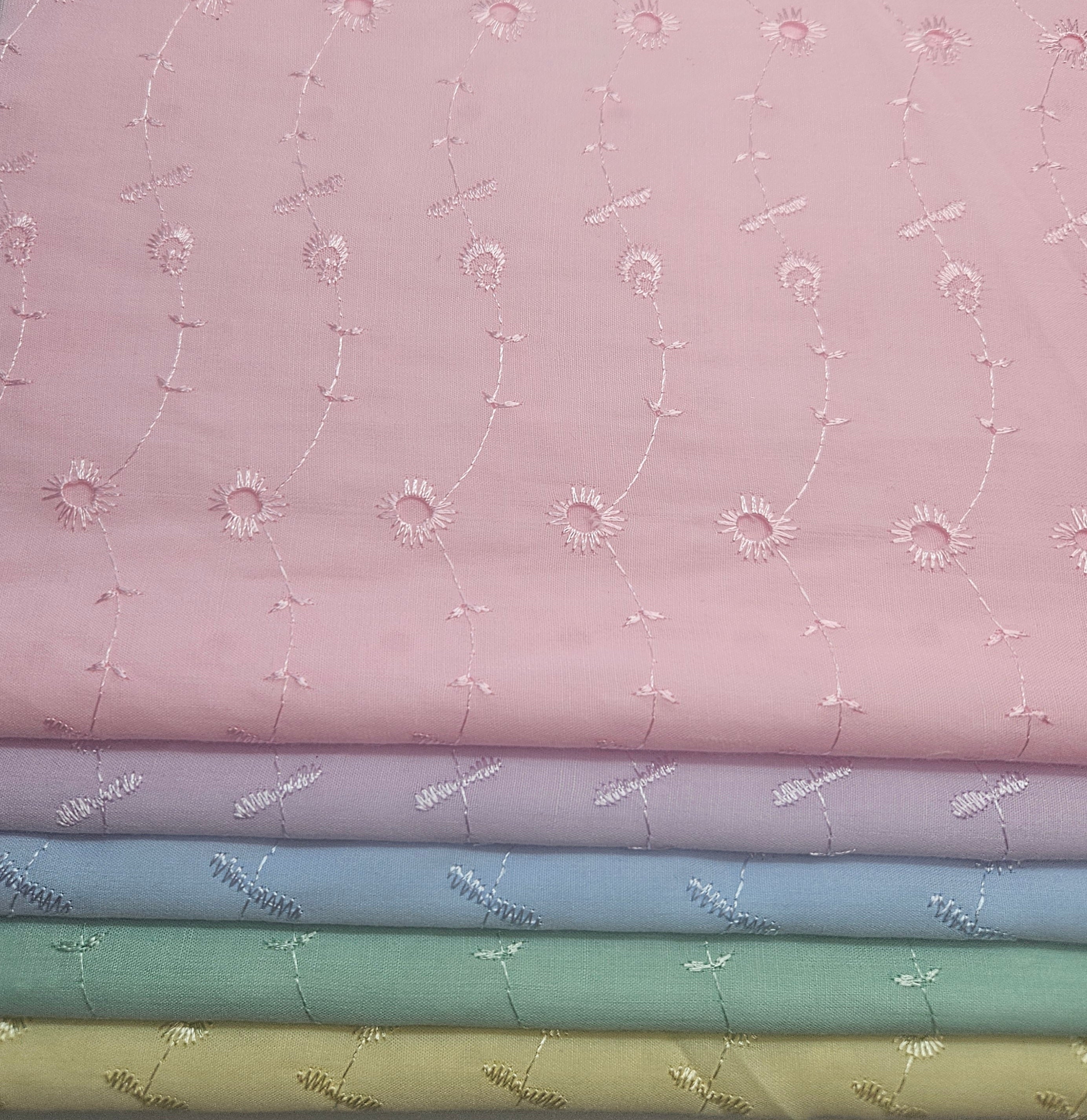 Stack of fabric swatches with floral patterns on a pink background