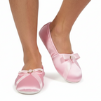 Pink satin shoes with bows worn by a person on a white background